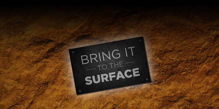 White text over black square label that reads: Bring it to the surface. Label is no a brown ground texture background